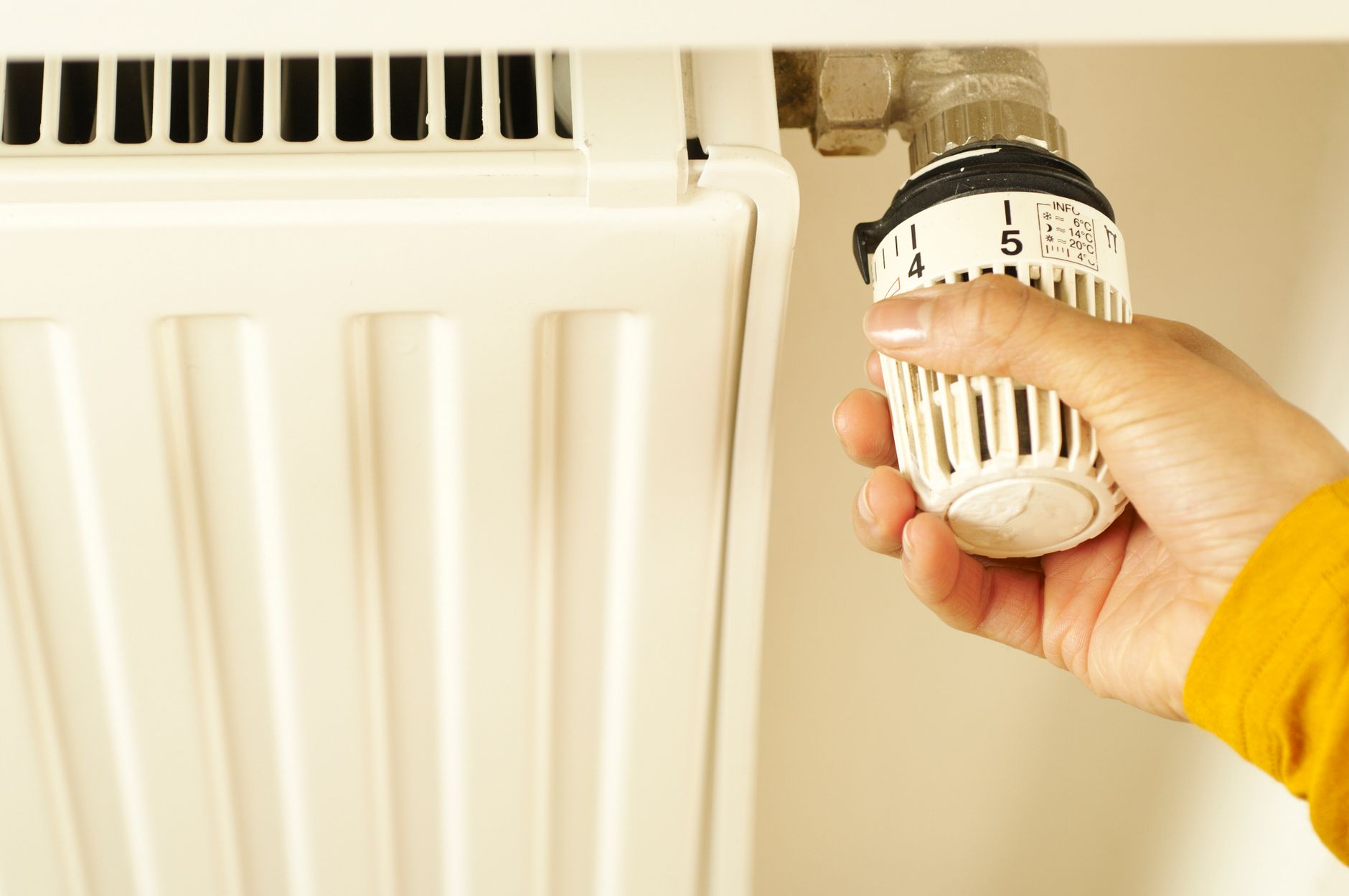 En hånd drejer på et termostathoved på en hvid radiator